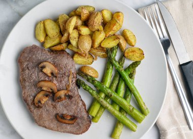 Mantarlı biftek, kuşkonmaz ve patates dilimleri ile servis edilir.