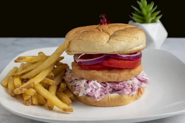 salmon burger  on cole slaw  with tomato and onion served with french fries.