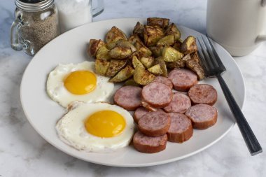  Kahvaltı tabağı kızarmış yumurta ve kızarmış patatesle servis edilen sosis.