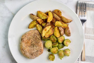 Kızarmış brussel lahanası ve patates dilimleriyle servis edilen kemiksiz domuz pirzolası.,