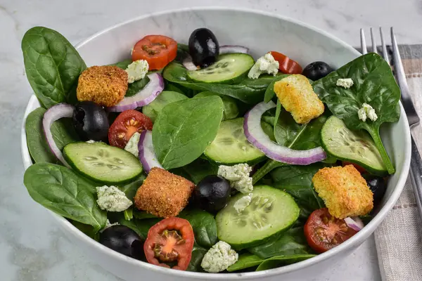 spinach salad consisting of cucumbers, tomatoes  and black olives