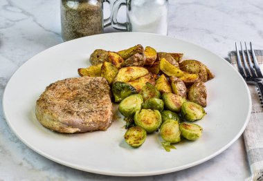 Kızarmış brussel lahanası ve patates dilimleriyle servis edilen kemiksiz domuz pirzolası.,