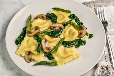 Sotelenmiş ıspanak mantarı ve kuşkonmaz ile servis edilen tavuk ravioli.