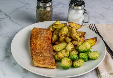 Patates dilimleri ve kızarmış brussel filizleriyle servis edilen baharatlı somon balığı.