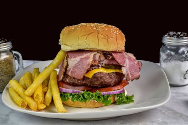 Domatesli pastırmalı peynirli burger ve patates kızartmasıyla servis edilen soğan.,
