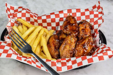 yanında patates kızartmasıyla servis edilen kanatlı babacue.