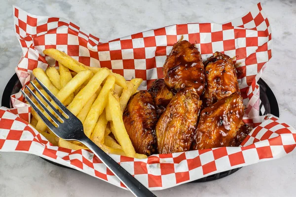 yanında patates kızartmasıyla servis edilen kanatlı babacue.