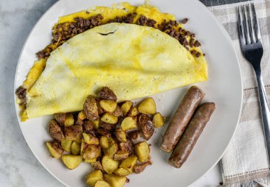 Kahvaltıda sosis ve patates kızartmasıyla servis edilen peynirli burger omleti.