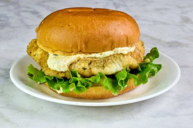 cod fillet sandwich  with lettuce and tarter sauce  served on a brioche bun clipart