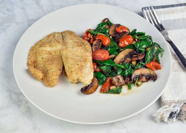  Kızarmış mezgit sotelenmiş ıspanak, domates ve mantarla servis edilir., 