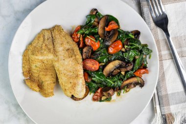 Kızarmış ıspanak, domates ve mantar yanında fırında mezgit.