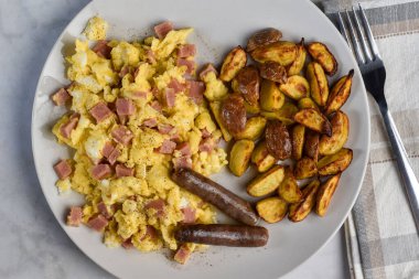 Konserve jambonla karıştırılmış yumurta, sosis ve yanında patates kızartması.
