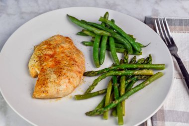 Baharatlı tavuk göğsü sotelenmiş yeşil fasulye ve kuşkonmazla servis edilir.,