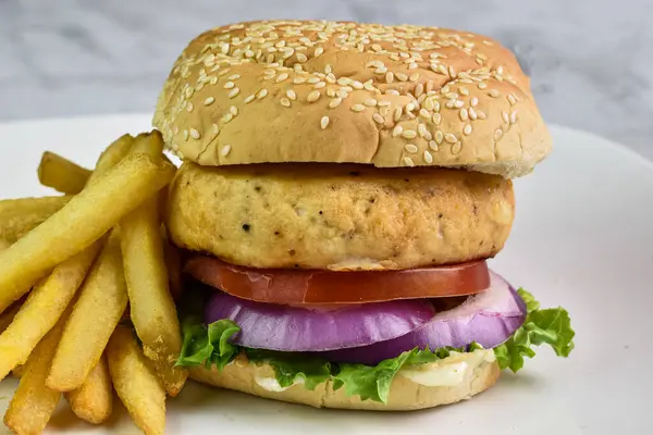 salmon burger resting on tomatoes onions and lettuce served on a sesame bun,