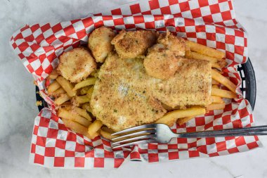 Fırında mezgit, deniz tarağı ve patates kızartması ile servis edilir.