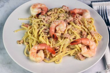 Alfredo soslu linguine kıyma ve karides ile servis edilir.,
