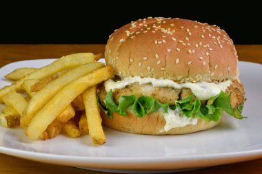 haddock fillet with  lettuce and tarter sauce on a sesame bun served with  fries clipart