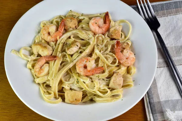 Sotelenmiş karides ve tavukla servis edilen linguine alfredo.