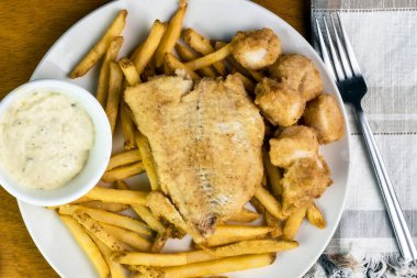 Fırınlanmış deniz tarağı ve patates kızartmasıyla servis edilen mezgit.