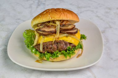 Susamlı ekmeğin üzerinde duran sulu peynirli burgerin üstünde soğan ve mantar.