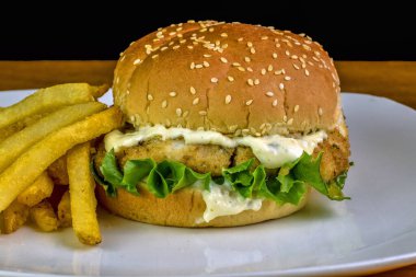 haddock fillet with  lettuce and tarter sauce on a sesame bun served with  fries clipart