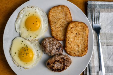 İki sauage köftesi ve kızarmış patates ile servis edilmiş yumurta.