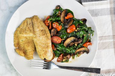 Kızarmış ıspanak, domates ve mantar yanında fırında mezgit.