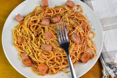 Konserve jambon, peynir ve maydanozla servis edilen soslu spagetti.,