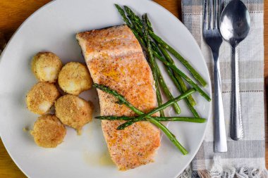 Fırında somon, deniz tarağı ve sotelenmiş kuşkonmazla servis edilir.