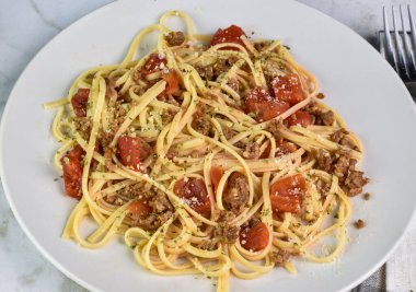 Doğranmış domates, parçalanmış sosis ve maydanozla servis edilen linquine..