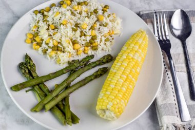 Mısır ve bezelye ile karıştırılmış pirinç asparaus ve mısır ile servis edilir.