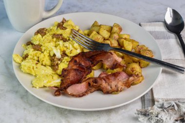 Domuz pastırması ve kızarmış patatesle servis edilmiş sosisli omlet.,