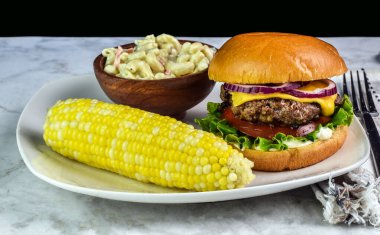 Peynirli ve soğanlı hamburger üstü makarna ve mısır., 