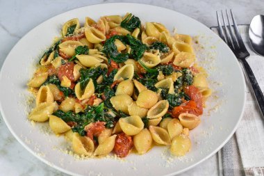 Sotelenmiş ıspanak ve domatesle servis edilen makarna kabukları.