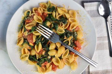 Makarna kabukları sotelenmiş ıspanak ve domates ile servis edilir.