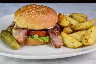 Domuz pastırmalı marullu domatesli sandviç, yanında patates kızartması ve turşu.