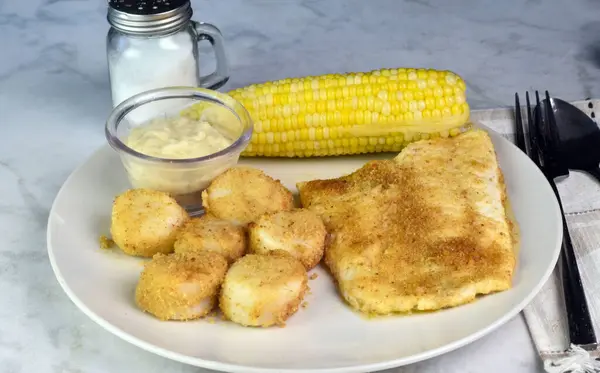 stock image baked haddock fillet served with baked scallops and corn on the cob.