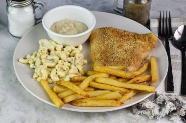 Fırında mezgit yanında patates kızartması ve makarna salatası.