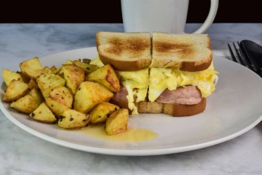 Konserve jambon ve çırpılmış yumurtalı sandviç ve yanında patates kızartması.