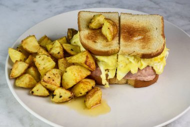 Yağda yumurta ve kızarmış patatesli jambonlu kahvaltı sandviçi.