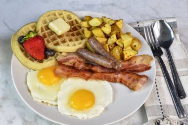 Pastırmalı sahanda yumurta, waffle ve patates kızartması ile servis edilen sosis.