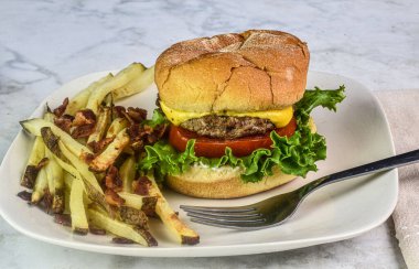 Domuz pastırmalı ev yapımı patates kızartmasıyla servis edilmiş, marullu ve domatesli peynirli burger.