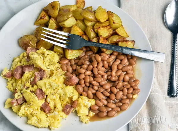 stock image scramble eggs  with  diced spam and pepper served with  baked beans and home fries.