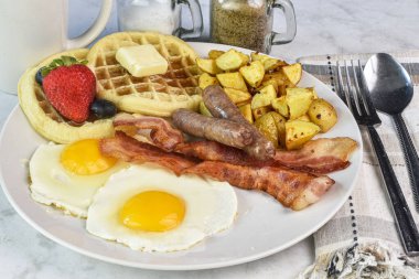 Pastırmalı sahanda yumurta, waffle ve patates kızartması ile servis edilen sosis.