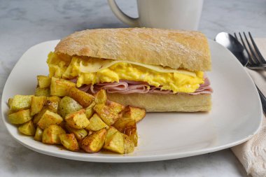 Çırpılmış yumurta, jambonlu ve peynirli sandviç ve yanında patates kızartması.