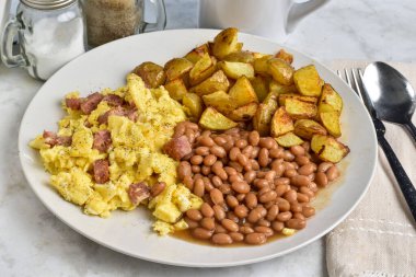 Karabiberli çırpılmış yumurta ve fırında fasulye ve patates kızartmasıyla servis edilen spamr..