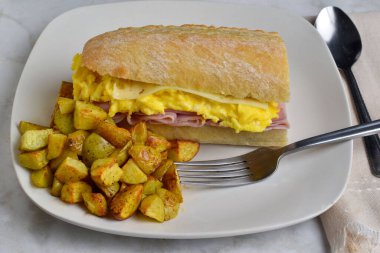 jambon, çırpılmış yumurta ve ciabatta sandviç ekmeğinde servis edilen İsviçre peyniri.,