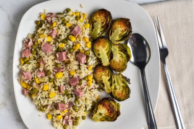 Pirinç kabuğu dilimlenmiş konserve jambon, mısır ve bezelye ile kızartılmış brussel lahanayla servis edilir.,