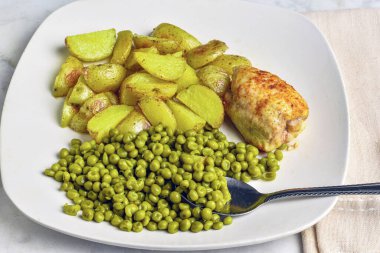  kızarmış tavuk butları patates dilimleri ve bezelye ile servis edilir..