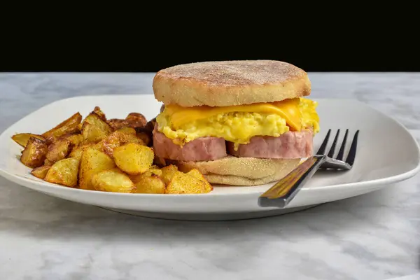 Konserve jambon, çırpılmış yumurta ve peynirli İngiliz çöreği ve patates kızartması.